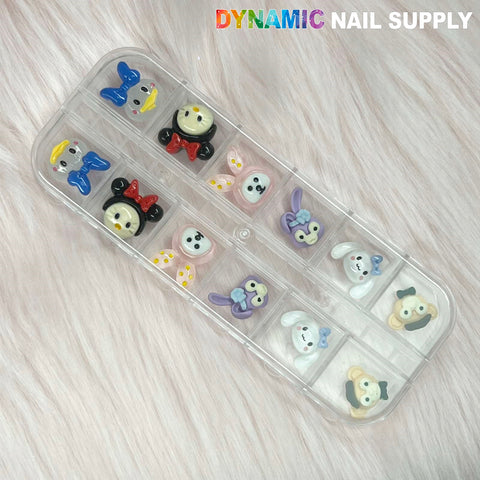 A clear case containing the Cartoon Characters Nail Charms set 03 is presented on a soft pink fur background. Each compartment highlights a distinct, colorful design that radiates playful whimsy. Ideal for nail art lovers, "Dynamic Nail Supply" is elegantly embossed in the top right corner.
