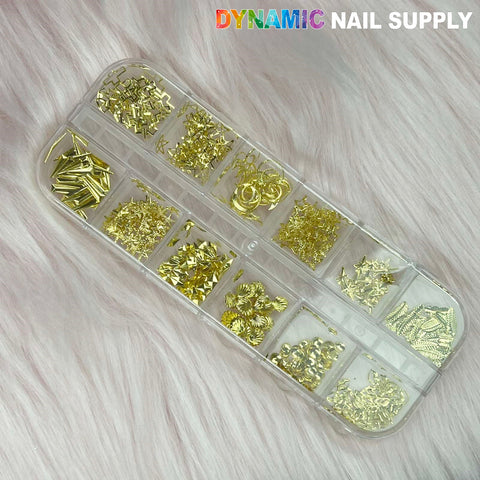 A clear plastic organizer holds twelve compartments, each containing an assortment of small gold nail art decorations such as studs, stars, and circles. This set, named "Nail Sequins and Rivet for Nails Designer set054," is ideal for enhancing any vibrant nail supply collection. It is showcased on a soft pink faux fur background with the "Dynamic Nail Supply" brand name printed in the top right corner.