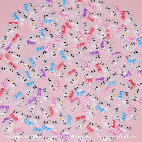 The "Mixed Colors" set from Dynamic Nail Supply includes 100 pieces of cute resin nail charms in the shape of cartoon cat faces. These charms feature whiskers and nose details, each embellished with colorful bows in shades of blue, purple, and pink. Set against a light pink background, this playful collection adds a Hell0 Kitty vibe to your manicure.