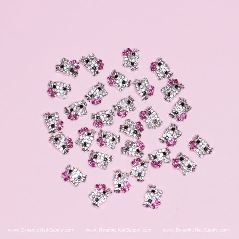 These metal Hello Kitty design nail charms from Dynamic Nail Supply feature a whimsical pattern scattered on a light pink background. Each charm is adorned with two pink rhinestones as bows and clear rhinestones on their bodies, offering a playful touch. Made from zircon alloy, these silver metallic charms come in a set of 30 pieces, perfect to enhance any nail art with their cute cartoon cat resemblance.
