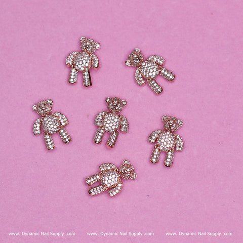 Six rose gold Teddy Bear charms from Dynamic Nail Supply, featuring rhinestones on a pink background. Each movable charm is adorned with shining stones for a glittery appearance. The bottom border displays "www.Dynamic Nail Supply.com" repeated twice.