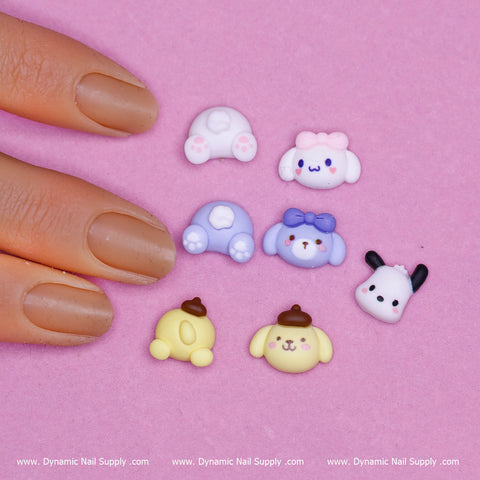 A painted nail points at seven vibrant nail charms on a pink background. These adorable charms, featuring cartoon characters like pastel sheep, cows, and puppies with playful expressions and accessories, are part of the "28 pcs Cute Cartoon Character charms for Nails Art Design" by Dynamic Nail Supply, whose brand name appears repeatedly at the bottom of the image.