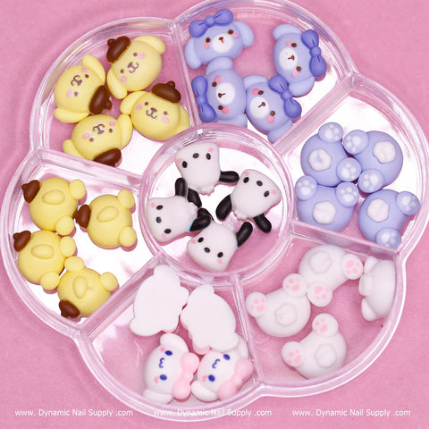 Dynamic Nail Supply offers a 28-piece collection of cute cartoon character charms for nail art design, housed in a round plastic organizer featuring a pink backdrop. The compartments are perfect for neatly organizing charming designs such as pandas, penguins, yellow bear faces, white animal faces with pink paws, and blue bows. Ideal for enhancing any nail art design!
