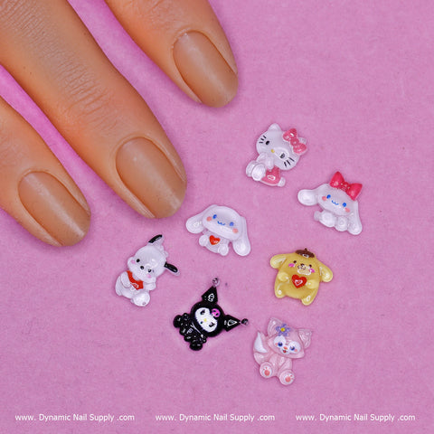 A hand adorned with nude nail polish rests on a pink surface surrounded by seven colorful cartoon resin charms shaped like adorable animals and characters, some embellished with bows and hearts. Along the bottom, the text "www.DynamicNailSupply.com" is repeated three times to highlight Dynamic Nail Supply's exclusive 70 pcs Hello Kitty resin charms for Nails Art Design.