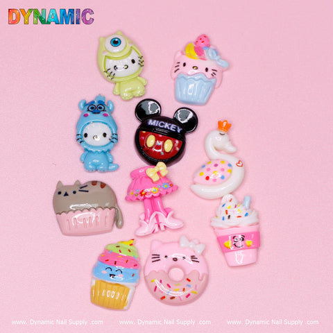 On a pink background, discover the adorable 10 pcs Cute Kawaii Cartoon Mixed Shape Design Nail Charms by Dynamic Nail Supply. These colorful charms include a cat donut, cupcake animals, Mickey Mouse head with Mickey, duck with a crown, llama, lamb, and ballerina outfit. The Dynamic Nail Supply logo is featured at the bottom.