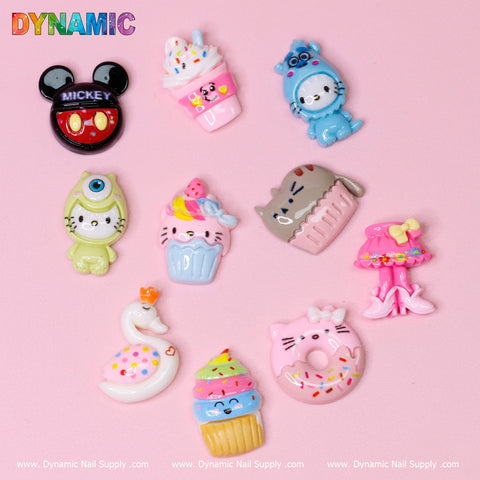 A vibrant assortment of 10 pcs Cute Kawaii Cartoon Mixed Shape Design Nail Charms from Dynamic Nail Supply, displayed on a pink background. The collection includes cartoon characters, cupcakes, and whimsical designs such as a pink skirt with a bow, a donut, a swan, and a Mickey Mouse badge. Each charm is colorful and intricately detailed.