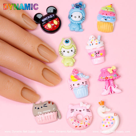 A hand with nude-colored nails showcases the "10 pcs Cute Kawaii Cartoon Mixed Shape Design Nail Charms" by Dynamic Nail Supply, featuring charming shapes such as a Mickey Mouse head, a blue bear, and a yellow monster. The scene is set against a pink background with the Dynamic Nail Supply logo positioned at the top left.