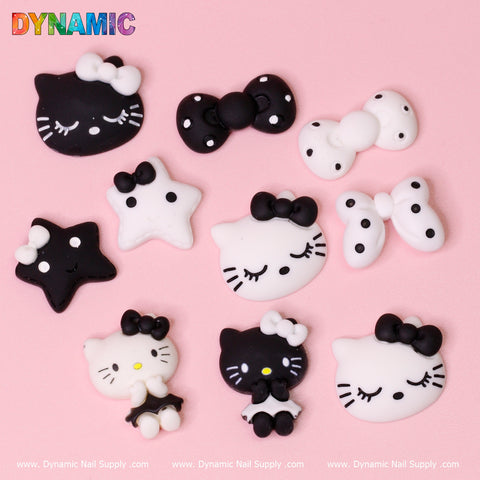A set of 10 cute Hello Kitty cat cartoon design nail charms from Dynamic Nail Supply is displayed on a pink background. These adorable pieces feature black and white cat faces, bows, and stars, with some decorated in polka dots and others in solid colors. The Dynamic Nail Supply watermark is visible.