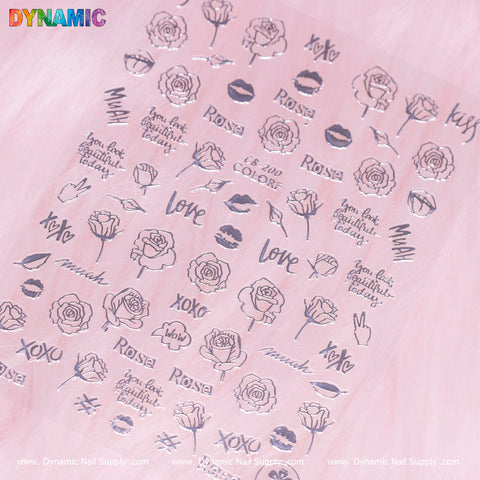 A sheet of transparent nail art stickers from Dynamic Nail Supply, featuring black line designs and silver accents on a pink background. The designs include roses, lips, love-themed words like "xoxo" and "kiss," along with phrases such as "you look beautiful today" in a hand-writing art style. Displayed at the top is the product name: hand writing art (silver) (CB 200).