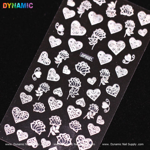A sheet of nail art stickers from Dynamic Nail Supply features intricate white designs of hearts, flowers, and roses set against a black background. The top left corner displays the word "DYNAMIC" in colorful letters, while the name Dynamic Nail Supply is printed in white text at the bottom.