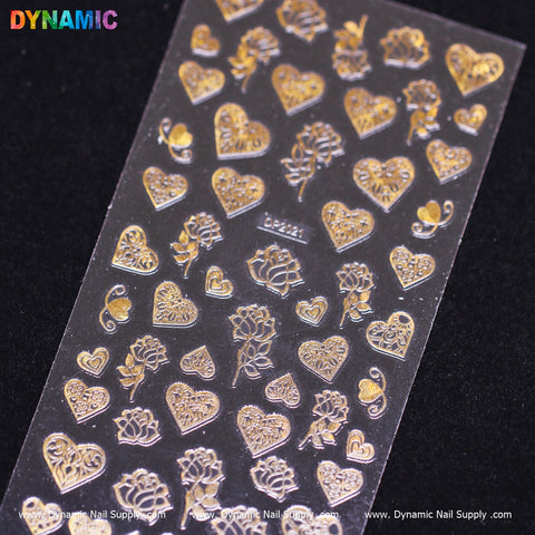 A sheet of heart, flower, and rose-themed rose gold nail art stickers from Dynamic Nail Supply, featuring intricate designs, is placed on a black surface. The stickers come in various sizes and patterns. The top left corner showcases the word "DYNAMIC" in vibrant letters, while the bottom edge lists www.DynamicNailSupply.com.