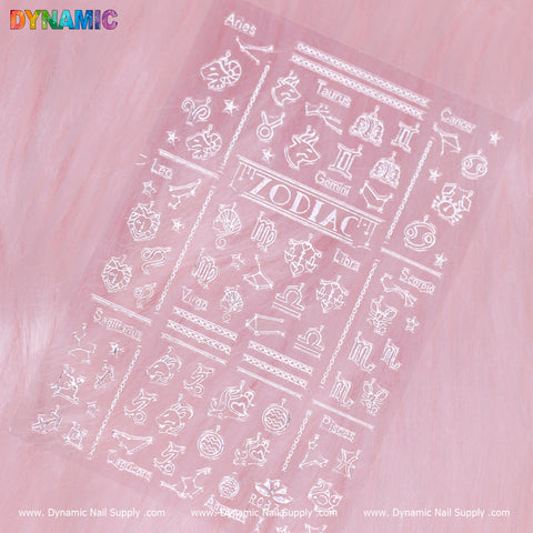 The Zodiac Sign (White) (R 087A) decal sheet from Dynamic Nail Supply showcases white zodiac signs and names on a pink background. Each sign is accompanied by its symbol, arranged in a grid layout, with the word ZODIAC prominently centered. The top and bottom feature the Dynamic Nail Supply logos.