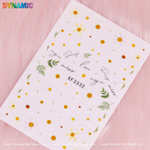 A sheet of nail stickers from Dynamic Nail Supply features vibrant yellow and orange daisies, delicate green foliage, and cursive text like dream, love, and magic. The design is complemented by a White Daisy Flower. At the center on a soft pink background, the code XF 3332 is visible.