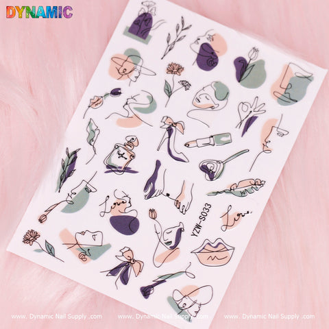 A sheet of minimalist nail stickers by Dynamic Nail Supply is displayed on a pink surface, featuring abstract line art of faces, plants, and hands in shades of green, purple, orange, and black. These designs include flowers and various hand gestures with intricate handwriting details and are marked with YZW S033 along the bottom edge.