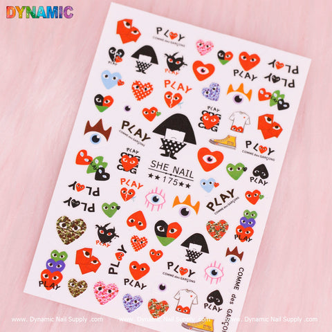 This product description features the Comme Des Garcons Sticker (175) by Dynamic Nail Supply, which includes a variety of nail sticker designs: red hearts with eyes, cartoon figures, abstract shapes, and the iconic Comme des Garçons PLAY logo. All these are elegantly displayed on a soft pink background.