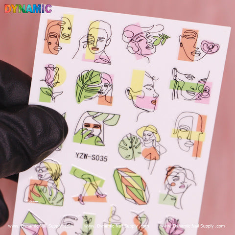 A gloved hand holds a sheet of Hand Writing (YZW S035) nail art stickers from Dynamic Nail Supply, featuring abstract female faces, leaves, and geometric designs. Predominantly pink, green, and orange, this product adds a vibrant touch to any manicure.