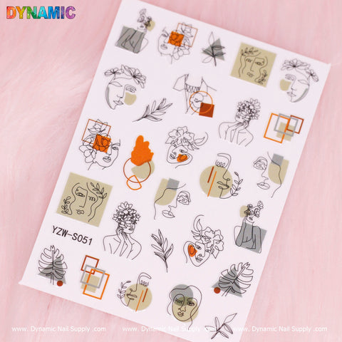A sheet of nail stickers from Dynamic Nail Supply's "Hand Writing" collection (YZW S051) is displayed on a pink surface. It features abstract line art depicting faces, plants, and geometric shapes in a palette of green, orange, and black against a lightly textured background.