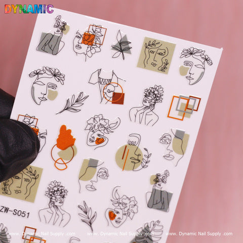 A gloved hand is holding a white sheet of nail art stickers labeled as Hand Writing (YZW S051) by Dynamic Nail Supply. The abstract design features minimalist line drawings of faces intertwined with floral elements, geometric shapes, and pastel shades such as green and orange.