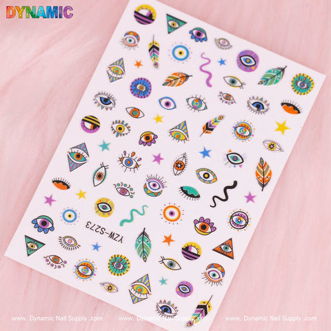 A sheet of vibrant nail decals, under the product name "Evil Eyes and Spirit styles (YZW S273)" from Dynamic Nail Supply, features a variety of eye designs, including open and closed eyes with lashes and abstract shapes. Some designs are embellished with teardrops, stars, and leaves against a soft pink background showcasing the Dynamic Nail Supply logo.
