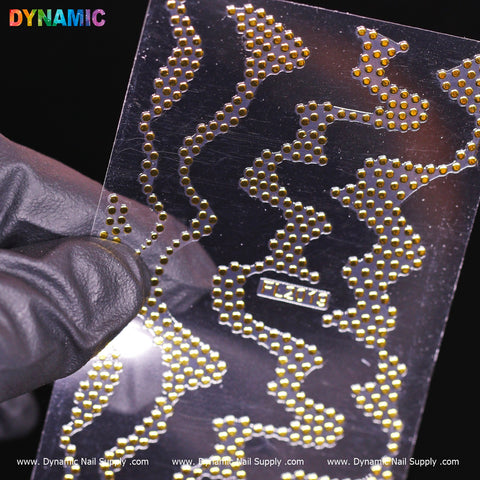 A gloved hand holds a transparent sheet showcasing Gold dot pattern art and wavy designs against a dark background. The sheet, identified as FL 2019, features small round designs. The brand Dynamic Nail Supply is prominently displayed at the bottom edge.