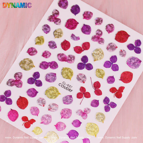 A sheet of nail art stickers from Dynamic Nail Supply, titled "Purple Pink Red Leaves (CL 037)," showcases a vibrant assortment of leaf designs in purple, red, and pink hues. The patterns shimmer with hints of gold against a soft pink backdrop.