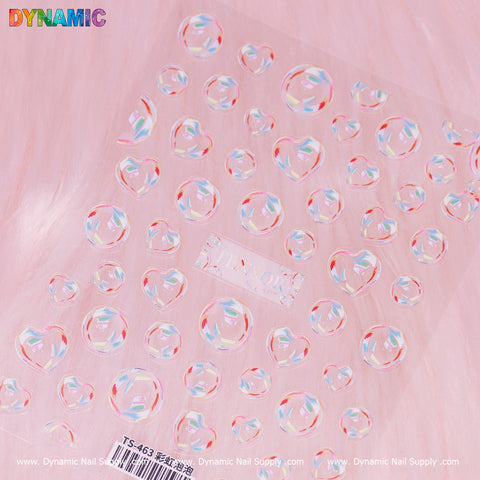 The 3D Bubbles Iridescent stickers (TS 463) from Dynamic Nail Supply are transparent and heart-shaped, organized in rows to mimic 3D bubbles. They sit atop a soft pink furry background, reflecting vibrant, shimmery hues while the brand name "Dynamic Nail Supply" and product code "TS 463" subtly repeat along the bottom edge.