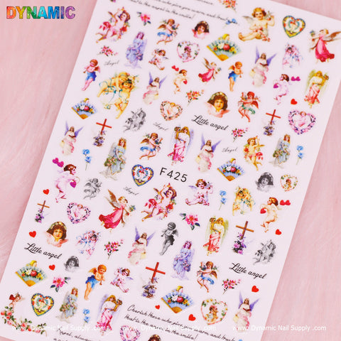 A sheet of white nail decals from Dynamic Nail Supply, featuring the Angel, Cupid, Holy and Christian style (F425) designs. These decals showcase cherubs, floral arrangements, hearts, and the text "Little angel" in an enchanting Christian style. The collection includes small angels playing instruments, holding flowers, and in playful poses. Additional elements consist of crosses and colorful butterflies.