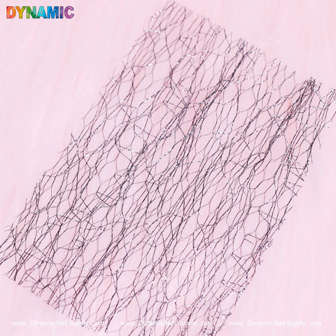 Displayed on a light pink background is a piece of the Seamless Mesh Pattern from Dynamic Nail Supply. This abstract design showcases diamond-shaped details within a fishnet mesh, resulting in a textured, lace-like appearance. The soft and delicate colors provide an appealing contrast between the dark mesh and the pastel backdrop.