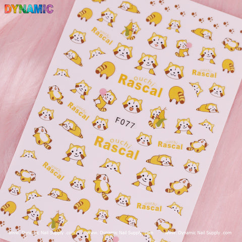 Sticker sheet featuring charming cartoon illustrations of cute red pandas, frequently confused with raccoons, in various playful poses and expressions. The text includes "Rascal" and "Ouchi Rascal!" arranged in a whimsical pattern. The design is set against a pink textured background, with the Dynamic Nail Supply brand name displayed above and their website below. This product is known as the Ouchi Rascal Racoon Cartoon (F077).