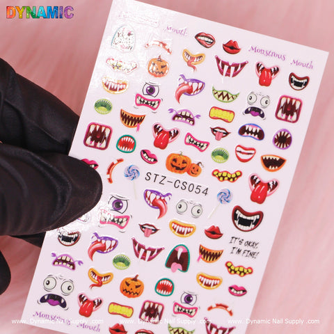 On a pink background, a sheet of Halloween-themed nail stickers called Monstrous Mouth Sticker (STZ-CS054) is displayed. Highlighting vibrant designs of monstrous mouths, bright pumpkins, and fangs, it is centered by a gloved hand. The brand Dynamic Nail Supply is prominently shown at the bottom.