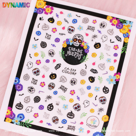 Dynamic Nail Supply's Day of The Dead, Skull Sticker sheet (Design code: CA-339) features colorful skull stickers alongside pumpkins, ghosts, spider webs, and flowers. It also includes phrases like "Trick or Treat" and "Day of The Dead." The background is white with a pink border.