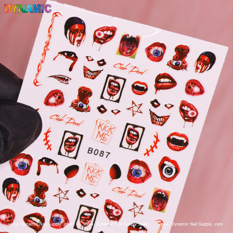 A hand sporting a black glove holds a sheet of Dynamic Nail Supply's Bloody Halloween Sticker (B087) decals against a pink backdrop. The designs include red lips, eyes, skulls, and playful phrases like "Kick Me" and "Club Dead," with additional bloody themed stickers such as red stars and drips encircling the central code B087.