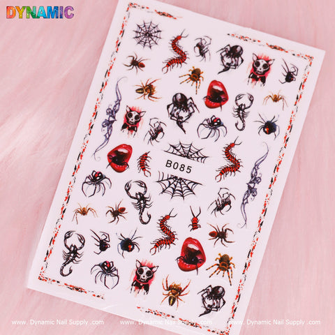 A sheet of Creepy Halloween Sticker (B085) lies against a pink background, featuring designs of spiders, webs, skulls, scorpions, vampire lips, and blood splatters. It's bordered in red with the Dynamic Nail Supply logo prominently displayed in the top left corner.