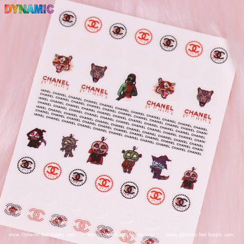 A sheet of Luxury Halloween Stickers by Dynamic Nail Supply, model T-589, on a pink background features comic-style animal faces and characters with interspersed text CHANEL, red Chanel logos, and a festive Halloween sticker for added flair.