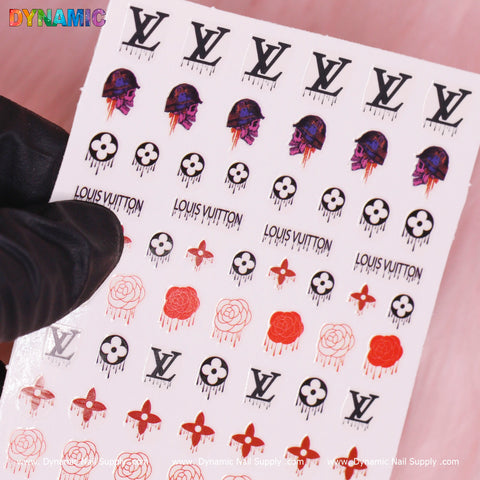 Against a pink background, a hand in a black glove holds a sheet of Dynamic Nail Supply's Luxury Halloween Sticker (T-586), showcasing designs such as Louis Vuitton logos and Halloween-themed stickers like skulls, roses, and mushrooms in black, red, and purple.