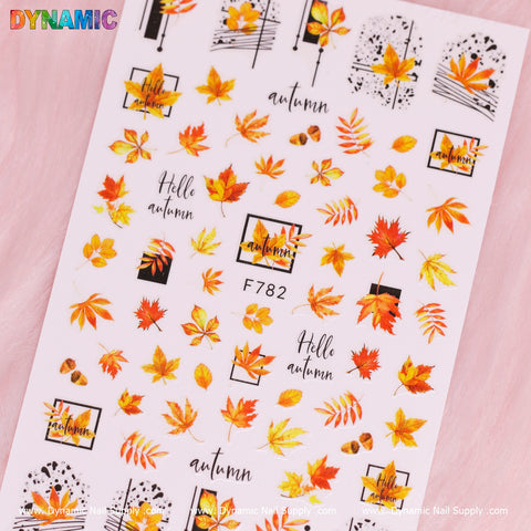 Presenting the Autumn, Fall Leaves Sticker (F782) by Dynamic Nail Supply—a set of nail stickers that beautifully captures the essence of the season with vibrant fall leaves, branches, acorns, and cursive text such as "Hello Autumn." These stickers are elegantly arranged on a pink background with Dynamic Nail Supply branding positioned at the top left corner.