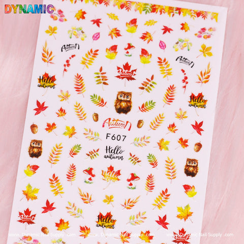 A sheet of the Autumn, Fall Leaves Sticker (F607) by Dynamic Nail Supply features vibrant nail stickers depicting fall leaves, acorns, owls, and mushrooms along with the phrase "Hello Autumn." The design is filled with rich reds, oranges, yellows, and browns set against a soft pink background and complemented by Dynamic Nail Supply's lively logo.