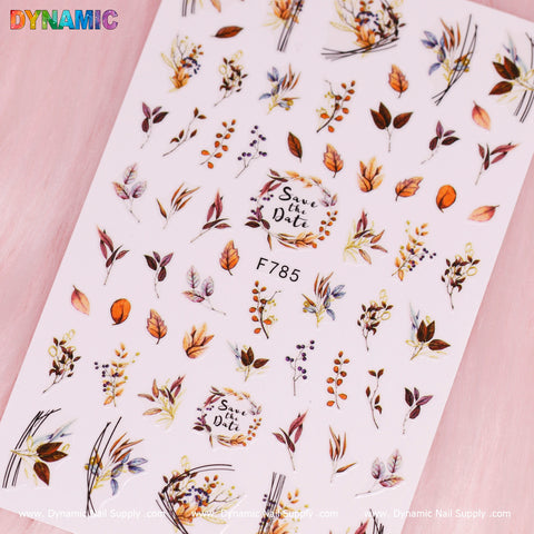 A sheet of Dynamic Nail Supply's Autumn, Fall Leaves Sticker (F785) displays colorful fall leaves and floral patterns in warm shades of orange, brown, and yellow. Decorative circles with "Save the Date" phrases are set against a soft pink backdrop. The charming sticker collection proudly features the code F785.