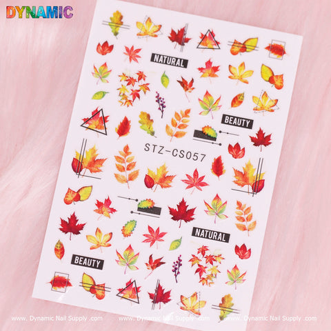 A sheet of nail art stickers is set against a pink background, featuring vibrant autumn leaves in shades of red, orange, and yellow. The words "NATURAL" and "BEAUTY" are displayed in black text. At the center is the code STZ-CS057, surrounded by Dynamic Nail Supply logos at the top and bottom. Ideal for a fall-inspired manicure, this product is officially named Autumn, Fall Leaves Sticker (STZ-CS057) by Dynamic Nail Supply!