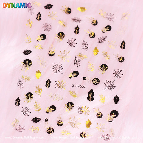 A pink background highlights diverse gold and black nail art decals, featuring cannabis leaves, geometric shapes, and abstract patterns. The word DYNAMIC bursts into view in a colorful gradient at the top-left corner. Taking center stage is the Gold and Black Autumn, Fall Leaves Sticker (Z-D4005) from Dynamic Nail Supply, offering an autumn-inspired elegance.