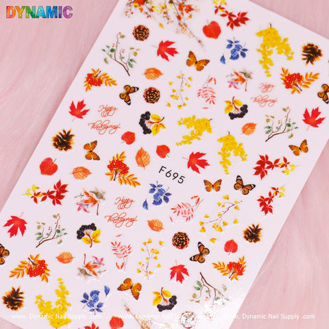 The Autumn, Fall Leaves Sticker (F695) by Dynamic Nail Supply features a pink base adorned with vibrant autumnal elements such as orange, red, yellow, and brown leaves, as well as butterflies, acorns, pinecones, and flowers. Charming cursive text reading "Happy Fall Y'all" completes the design.