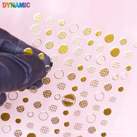 A hand in a black glove holds a transparent sheet of Dynamic Nail Supply's "Polka Dot, Circle Abstract Sticker (DP3215)," showcasing gold polka dot and grid designs against a light pink background. The sheet offers both solid circles and mesh-like patterns, with the brand name "DYNAMIC" displayed in colorful letters at the top left corner.