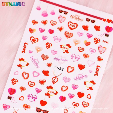 The Love Heart Sticker (F632) from Dynamic Nail Supply includes heart designs, lip prints, love-themed texts, and "Happy Valentine's" phrases. These stickers showcase a variety of sizes and designs in red, pink, and white shades against a light pink background.