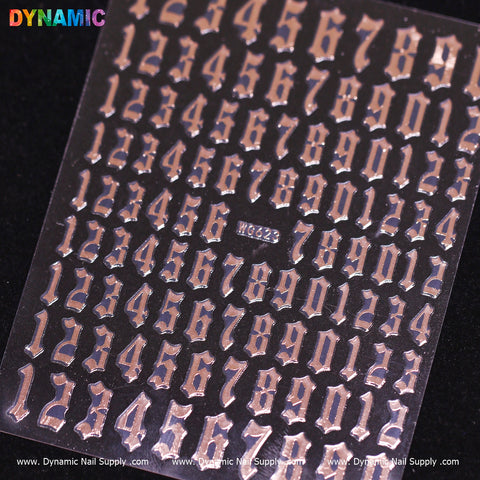 A rose-colored sheet showcases metallic silver adhesive numbers in a Gothic font, arranged in rows. The Number Sticker includes digits 0 through 9, repeated multiple times. The top left corner features Dynamic Nail Supply's colorful logo, while the bottom edge displays www.DynamicNailSupply.com and the model number WG623 repeatedly.