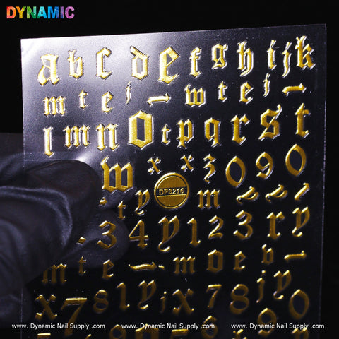 A sheet of gold stickers titled "Letter and Number Sticker (DP3216) - Gold" by Dynamic Nail Supply, showcasing Gothic-style letters and numbers. The set contains the complete alphabet from a to z along with numbers 0 through 9. A gloved hand supports the sheet at the bottom left corner, with "Dynamic Nail Supply" appearing repeatedly along the lower edge.