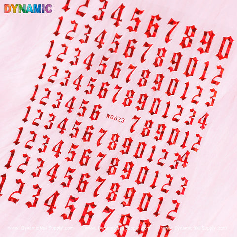 A variety of red Number Stickers (WG623) from Dynamic Nail Supply in a gothic font are scattered across a light pink background. The alphanumeric code WG623 is prominently displayed at the center, and the top left corner features the word DYNAMIC in multicolored text.