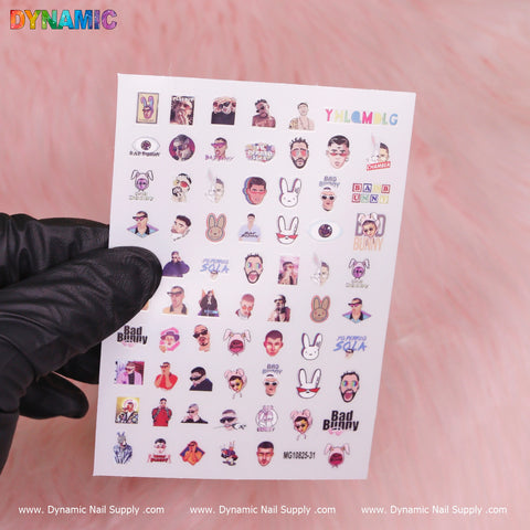 A gloved hand displays a sheet of Dynamic Nail Supply's Bad Bunny Hip Hop Sticker (MG10825-31), featuring an array of colorful cartoon designs such as characters sporting sunglasses, playful rabbits, and text proclaiming “Bad Bunny.” This is set against a gentle pink background.