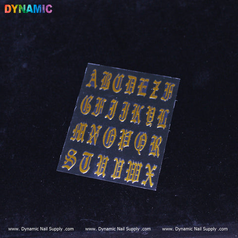 A sheet of Roman Alphabetical Sticker (Gold) showcasing uppercase Old English font shines brilliantly with a black outline. Set against a dark surface, the sheet distinctly features Dynamic Nail Supply's logo repeated along the bottom edge, accentuating its luxurious design.