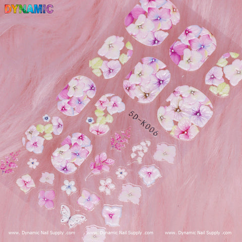 The Floral Sticker (5D-K006) from Dynamic Nail Supply showcases pastel hydrangea designs in pink, purple, and white hues. The sheet includes a butterfly and small crystal-like details on a gentle, fluffy pink background, with "Dynamic Nail Supply" embossed repeatedly along the bottom edge.