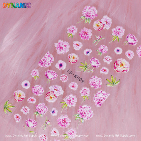A set of floral nail art stickers, labeled 5D-K009, showcases roses, peonies, and greenery arranged on a soft pink fur-like background. The brand name Dynamic Nail Supply is prominently displayed in colorful letters at the top left corner.